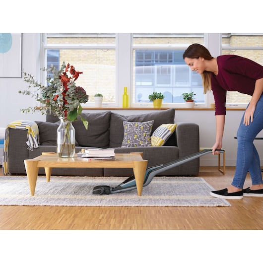 BLACKDECKER SVA420B vacuum cleaner being used under a coffee table in a modern living room.