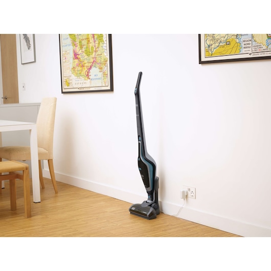 BLACKDECKER SVA420B cordless stick vacuum in black charging upright by a wall in a modern dining area.