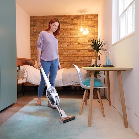 Photo of BLACKDECKER SVFV3250L cordless stick vacuum cleaner being used on a light blue rug in a bedroom.
