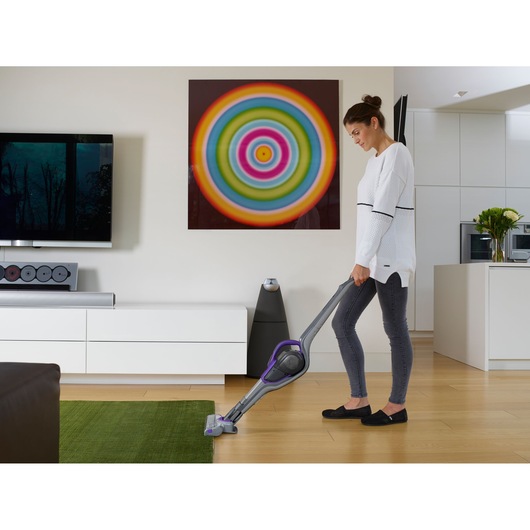 BLACKDECKER SVJ520BFSP cordless stick vacuum in use on hardwood and green rug in modern living room.