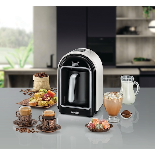 Photo of BLACK+DECKER TCM730 Turkish coffee maker on countertop with coffee cups, coffee beans, milk, and traditional sweets.