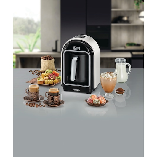 BLACKDECKER TCM730 coffee machine with silver pot, Turkish coffee cups, assorted sweets, coffee beans, and milk on table.