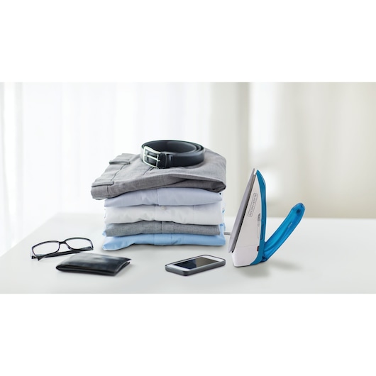 BLACKDECKER TI250 blue travel iron on table with folded clothes, belt, glasses, wallet, and phone.