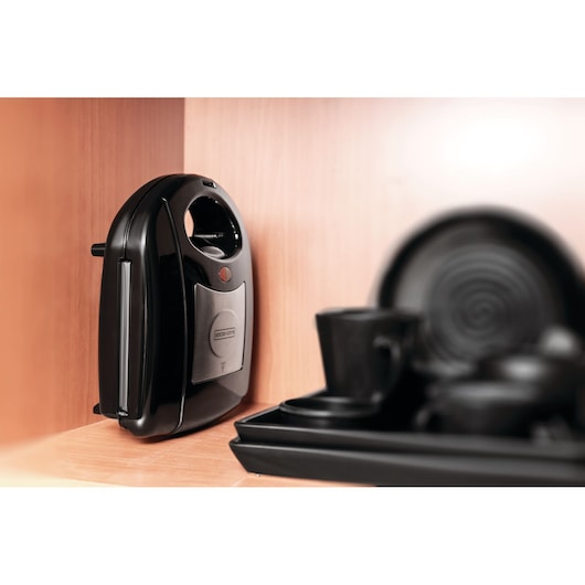 Photo of BLACK+DECKER TS2130 sandwich maker stored upright on a wooden kitchen shelf with black dishes nearby.