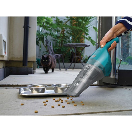 BLACK+DECKER WDB115WA handheld vacuum cleaning pet food near metal bowls, outdoor scene with black cat in background.