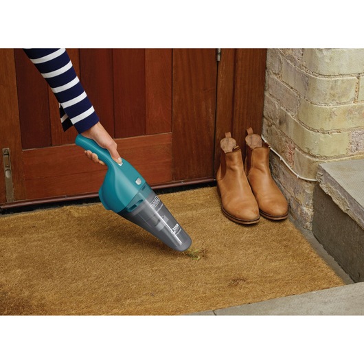 Photo of BLACKDECKER WDB115WA handheld vacuum used to clean a doormat near boots at a wooden door entrance.