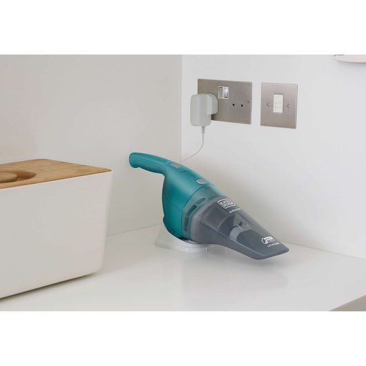 BLACK+DECKER WDB115WA handheld vacuum cleaner with teal body and transparent nozzle charging on kitchen countertop.