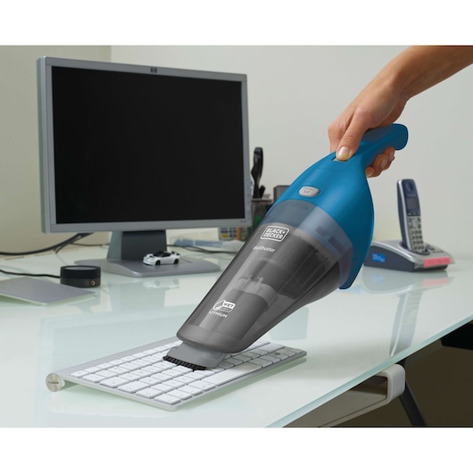 BLACK+DECKER WDB215WA handheld vacuum, blue and gray, cleaning computer keyboard on desk.