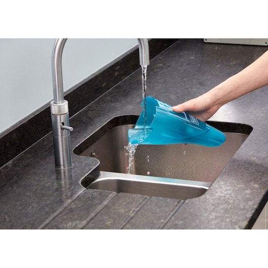 A person emptying water from a blue BLACK+DECKER vacuum cleaner container into a kitchen sink.