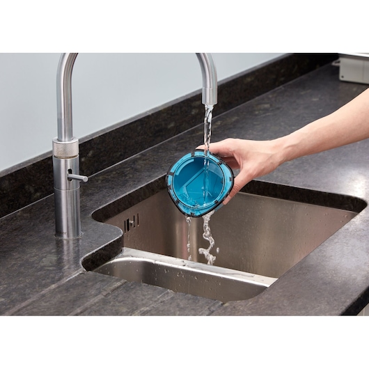A hand is rinsing a blue vacuum cleaner filter under running water in a kitchen sink.