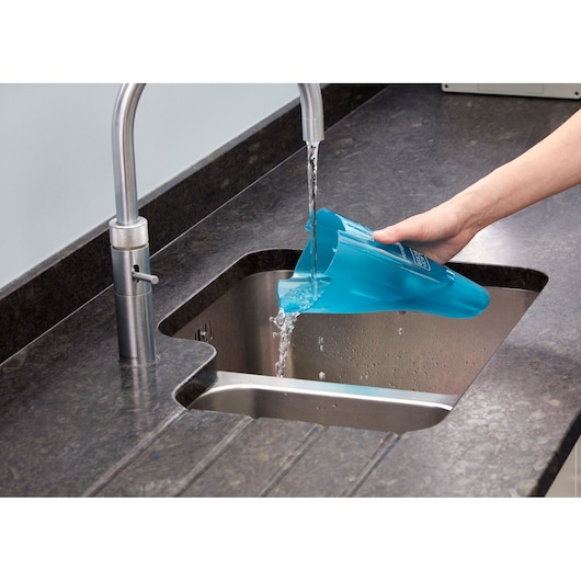 A person is emptying a blue BLACK+DECKER vacuum cleaner dust container into a kitchen sink under running water.