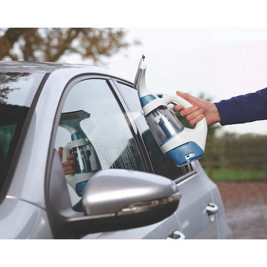 A person uses a BLACK+DECKER WW100 window vacuum cleaner to clean the exterior window of a silver car.
