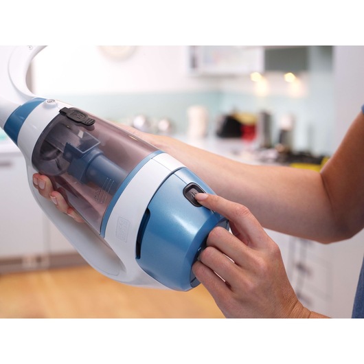 Close-up of a person holding and operating a handheld vacuum cleaner with a blue and white design in a modern kitchen setting.