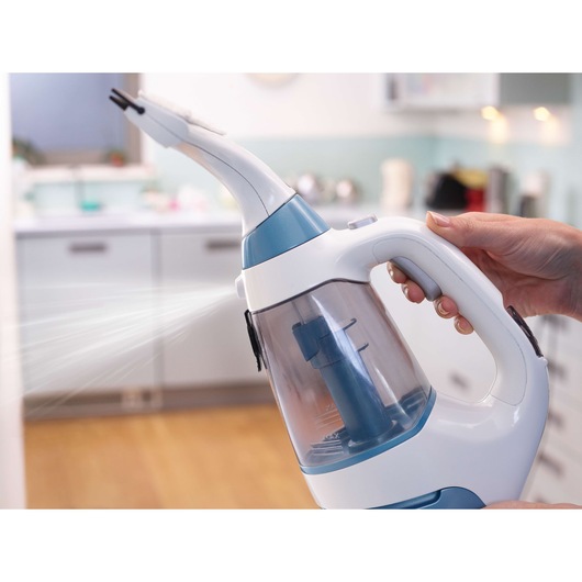 Close-up of a person using a handheld electric steam cleaner, spraying mist in a kitchen environment.