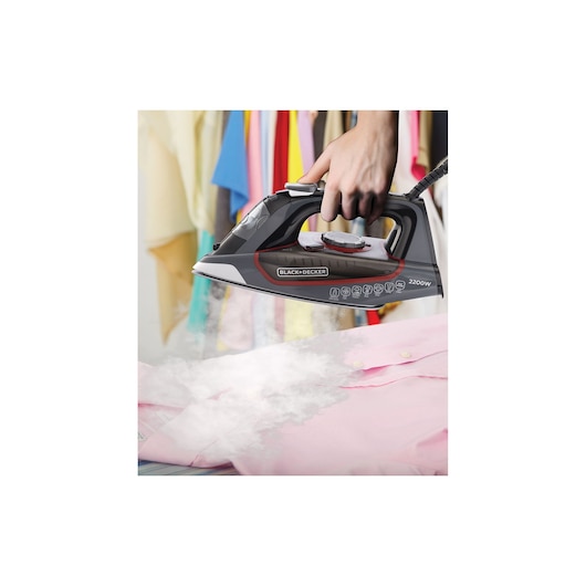Photo of BLACK+DECKER X2050 steam iron in use on a pink shirt with colorful clothes hanging in the background.