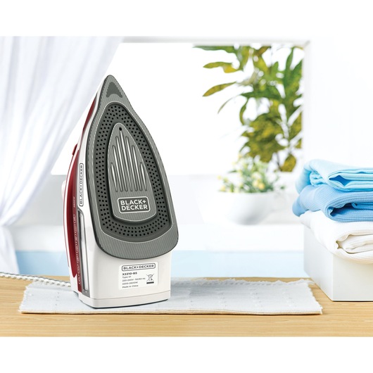 BLACK+DECKER steam iron X2210 upright on table near folded clothes, bright room background.