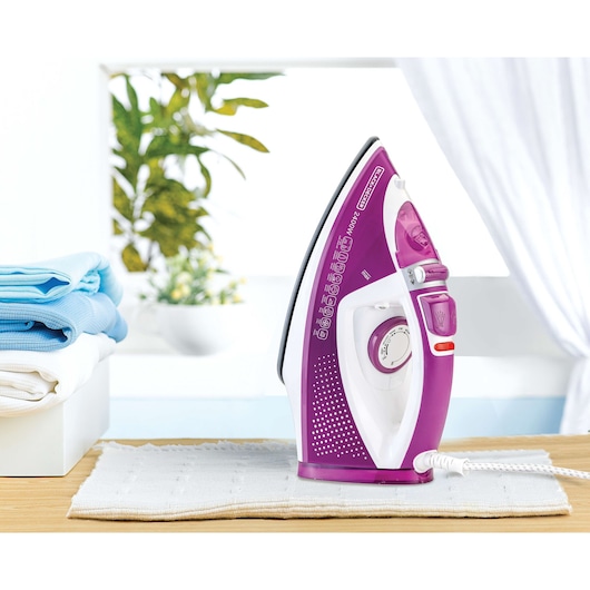 BLACKDECKER X2450 purple and white steam iron upright on cloth, side angle, laundry in background.