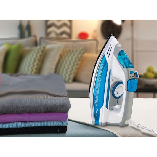 BLACK+DECKER X2800 steam iron with blue and white design, shown upright next to folded clothes in a home setting.